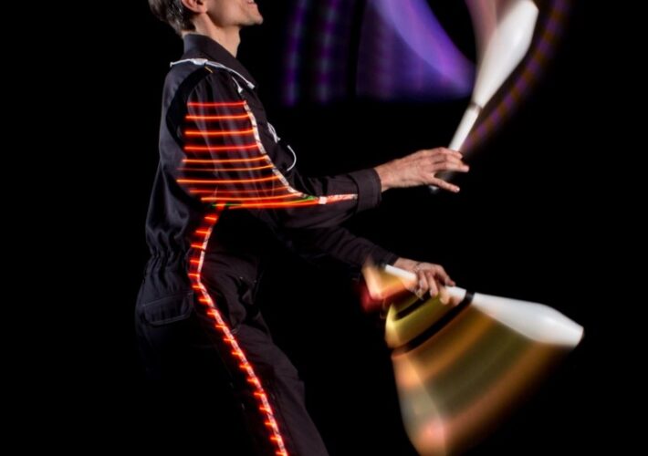 Markus Just jongliert mit drei leuchtenden Keulen in einem LED-Anzug