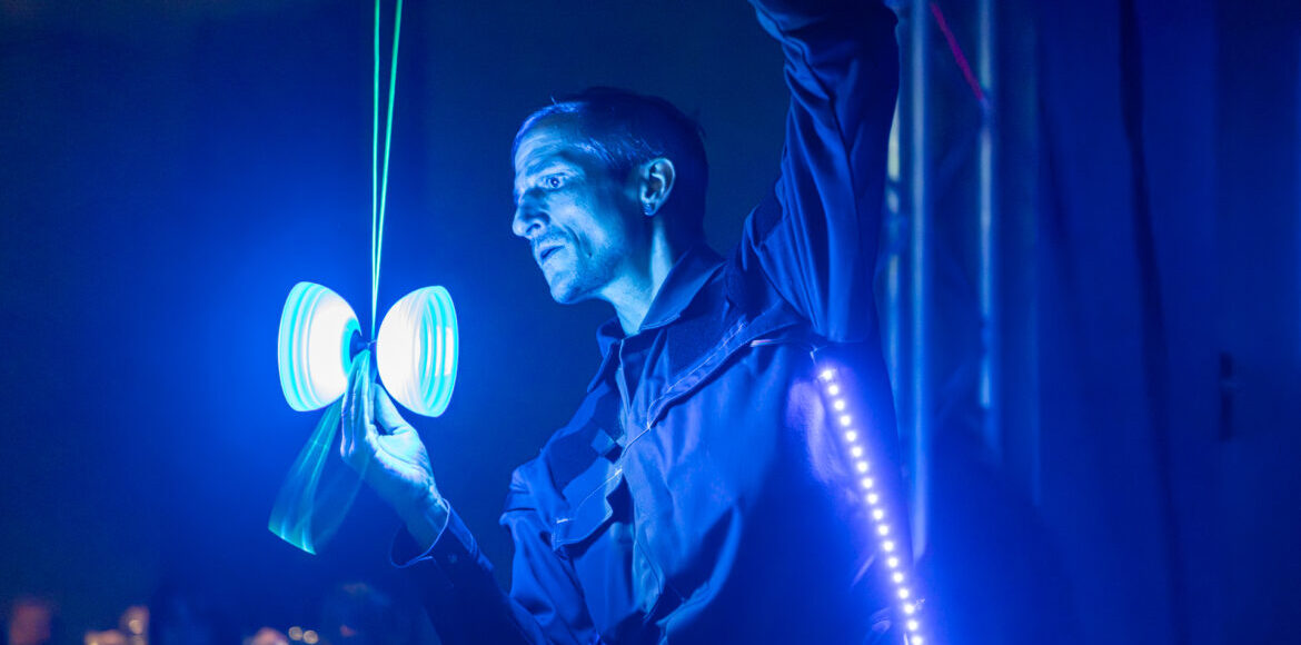 Künstler Markus Just in leuchtendem LED-Anzug balanciert ein strahlendes Diabolo auf der Hand während seiner LED-Show