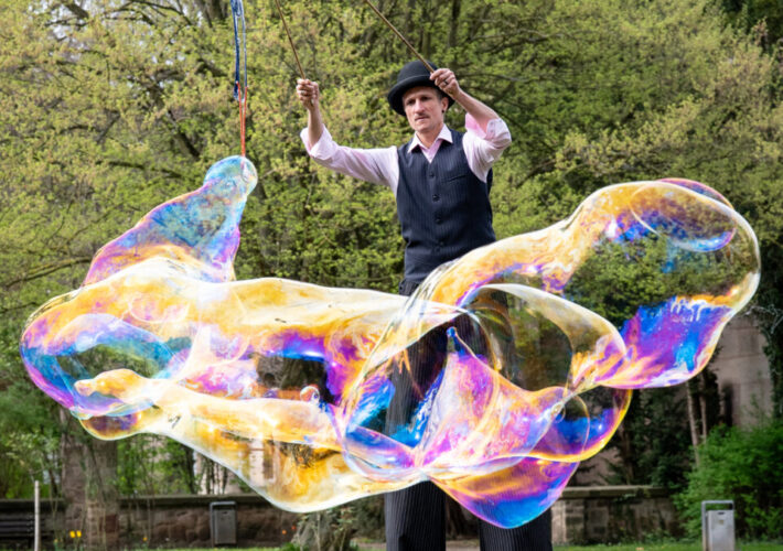 Künstler*in von justnonstop mit Riesenseifenblasen auf Stelzen bei einer Outdoor-Performance
