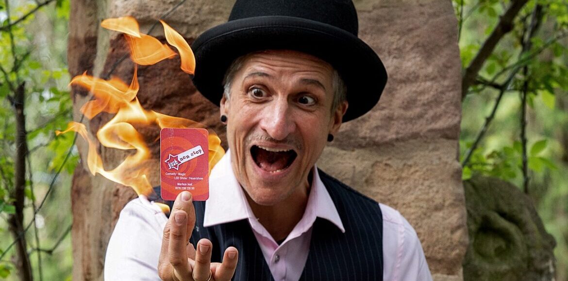 Zauberkünstler mit schwarzem Hut präsentiert eine Spielkarte vor einer Flamme.
