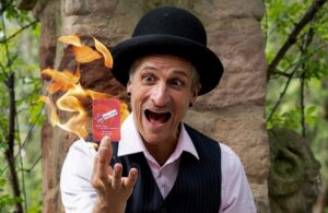 Zauberkünstler mit schwarzem Hut präsentiert eine Spielkarte vor einer Flamme.